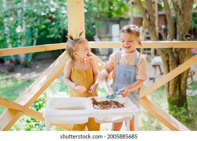 Happy Sister Kids Play With Sand And Water In Sensory Baskets On The Outdoor Sensory Table, Sensory Early Development, Montessori. Toddler And Big Sister Play With Sand, Soft Focus