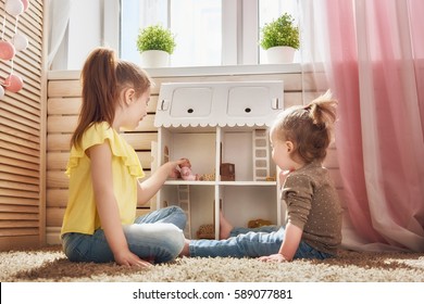 Happy sisters girls play with doll house at home. Funny lovely children are having fun in kids room.