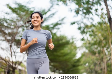 Happy Slim Woman Wearing Sportswear Jogging In The City At Sunrise. Young Beautiful Asian Female In Sports Bra Running Outdoor. Workout Exercise In The Morning. Healthy And Active Lifestyle Concept.