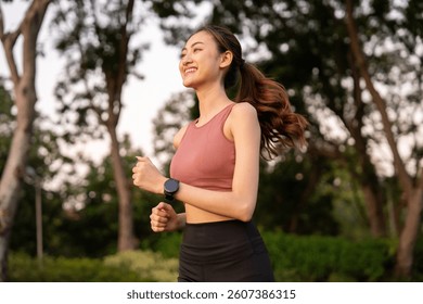 Happy slim woman wearing sportswear jogging in the city at sunrise. Young beautiful asian female in sports bra running outdoor. Workout exercise in the morning. Healthy and active lifestyle concept.