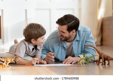 Happy small boy lying on floor with caring dad, enjoying funny conversation, discussing hand drawn pictures in living room. Emotional positive father involved in funny domestic activity with son. - Powered by Shutterstock