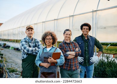 Happy small business owner and group of her workers in front of a greenhouse looking at camera. - Powered by Shutterstock