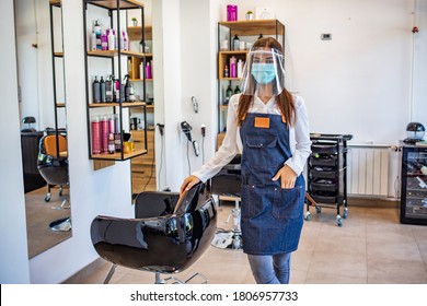 Happy small business owner at a hairdressing studio during COVID-19. Portrait of elegant hair salon employee in apron with medical mask, gloves, hair comb and scissors.