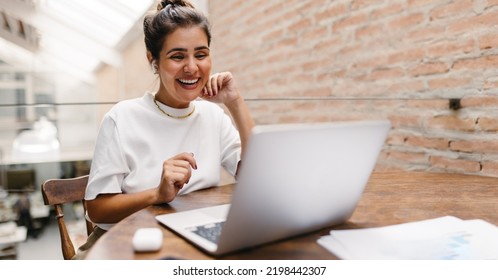 Happy Small Business Owner Having An Online Meeting In A Warehouse. Female Entrepreneur Video Calling Her Business Partners On A Laptop. Cheerful Businesswoman Running An Online Startup.