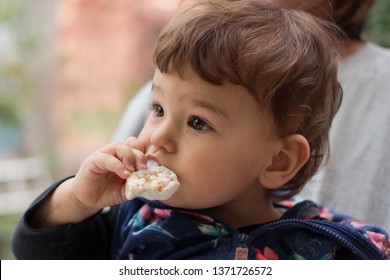 Happy small child sitting in mom's lap eating rice cake