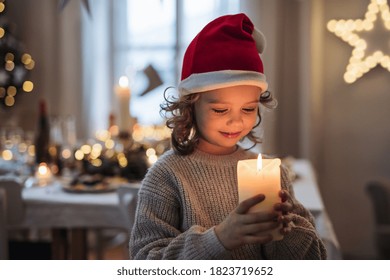 Happy small girl standing indoors at Christmas, holding candle.