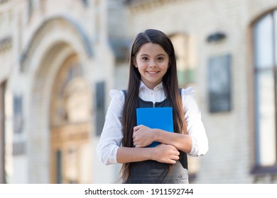 Happy small kid with school look wear uniform holding library book outdoors, knowledge.