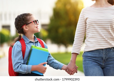 Happy smart girl with notebooks smiling and looking at crop mother while walking to school in green park together - Shutterstock ID 1799902393