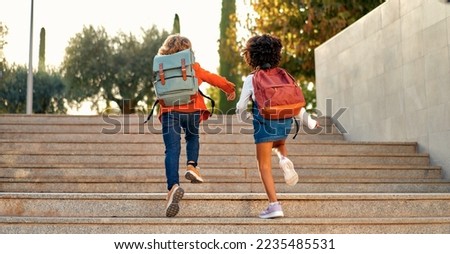 Happy smart kids with school bags rush to the lessons to school running up the stairs. Back to school. An African-American schoolgirl and her classmate walk down the street after school.
