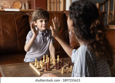 Happy Smart Little Boy Child Give High Five Play Chess Finish Set With Caring Mom At Home. Smiling Small 6s Kid Deal Celebrate Win Engaged In Board Game With Loving Mother. Creative Thinking Concept.