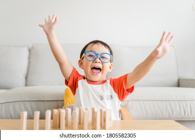 Happy Smart And Nerd Toddler Asian Boy Raised Hand When He Win Play Wooden Toy Block At Home.Boy Child Kid Wearing Glasses.myopia Or Short Sighted.Positive Human Emotion, Attitude And Self Esteem. 