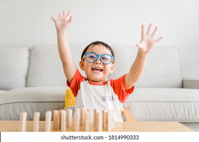 Happy Smart And Nerd Toddler Asian Boy Raised Hand When He Win Play Wooden Toy Block At Home.Boy Child Kid Wearing Glasses.myopia Or Short Sighted.Positive Human Emotion, Attitude And Self Esteem. 