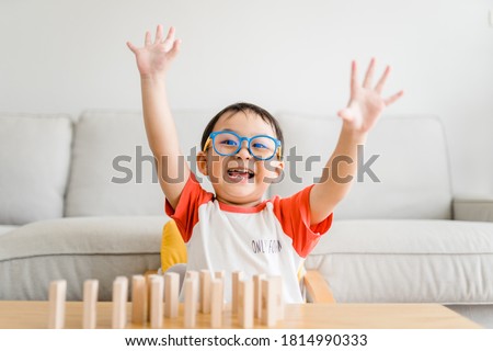 Happy smart and nerd toddler asian boy raised hand when he win play wooden toy block at home.Boy child kid wearing glasses.myopia or Short sighted.Positive human emotion, Attitude and self esteem. 