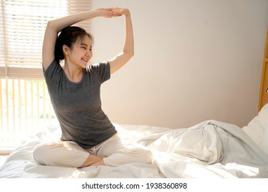 Happy Smile Asian Woman In Comfortable Pajamas Was Wriggling After Waking Up In Bed Near The Window That Was Shining In The Sun.