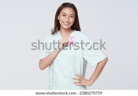 Happy smile asian woman patient showing pink badge ribbon chest to support breast cancer cause campaign. breast cancer awareness concept.
