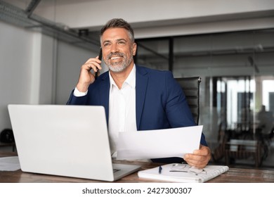 Happy smile Hispanic businessman talking phone and hear good news, checking database in office. Latin business man holding document, working at laptop computer doing online trade market tech research. - Powered by Shutterstock