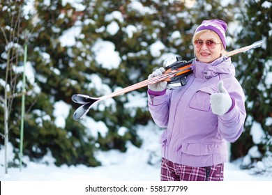 Happy And Smile Old Senior Woman Wearing Ski Jacket And Glasses With Skis On Shoulder. Showing Thumb Up