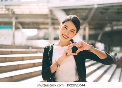 Happy Smile Young Adult Asian Business Single Woman Hand Up With Heart Gesture. Wear Silver Accessory And Charm For Lover Faith On Valentine Day. City People Lifestyle Concept.