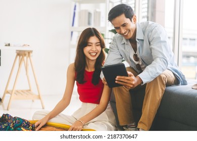 Happy Smile Young Adult Southeast Asian Couple Getting Ready For Holidays Travel Trip. Man Using Digital Tablet For Plans Talking With Woman. Living Room At Home Or Hotel Window Light.