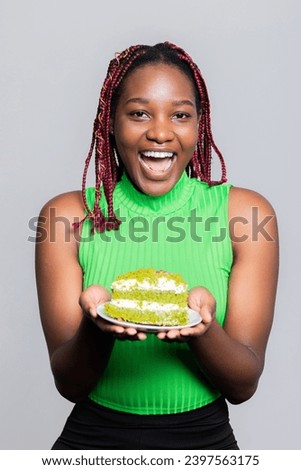 Happy smiley baker African American dark skinned baker woman with colourful braids smiling standing in the studio wearing casual outfit holding selfmade delicioua tasty cake in hands shop adverb.