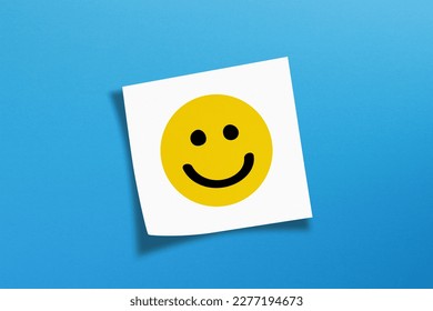 Happy smiley face emoticon with white note paper on blue background