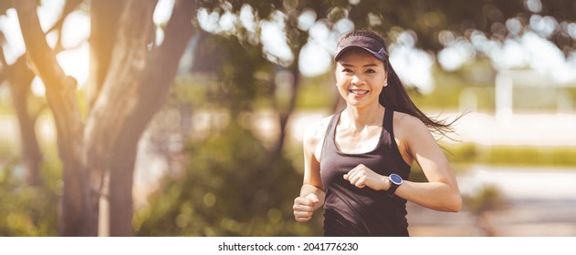 Happy Smiling Adult Asian Woman Jogging Outdoor In The City Park In Sunshine Beautiful Summer Day.  Happy Relaxed Mature Woman Jogging To Live An Active And Healthy Lifestyle