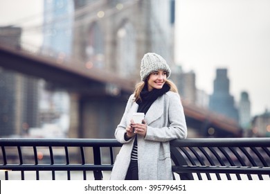 Happy smiling adult tourist woman holding paper coffee cup and enjoying the New York City view and Brooklyn bridge - Powered by Shutterstock