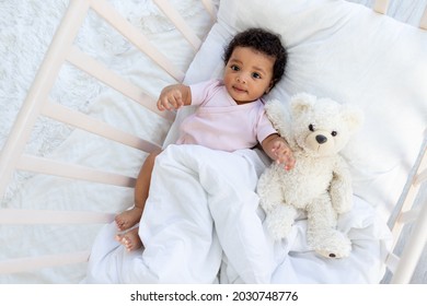 happy smiling african american baby in a crib with a teddy bear falls asleep or goes to bed
