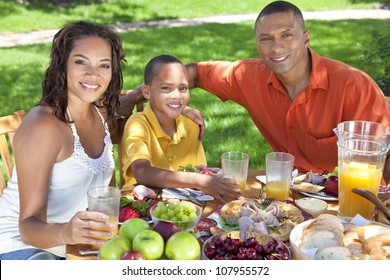 A Happy, Smiling African American Family, Mother Father & Son Eating Healthy Food At A Table Outside, The Father Is Serving A Orange Juice To The Boy.