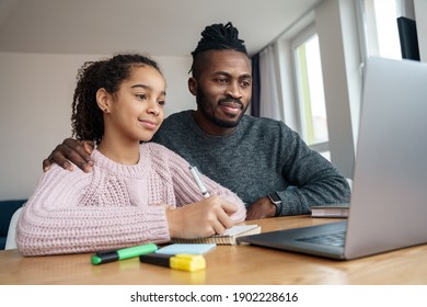 Happy smiling African American father helps to study online to his teen age nice daughter. E learning at home at quarantine by web camera. Family watch online course, webinar, online teacher in app. 