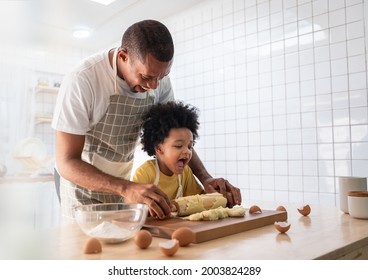 Happy Smiling African American Father and Adorable Son have fun Cooking and kneading dough in white kitchen. Playful Black Family baking cookies together at home.
