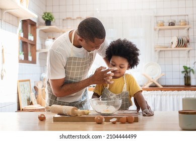 Happy smiling African American Father playing touching his little boy nose with flour while doing bakery at home, Black family having fun cooking baking cake or cookie in the kitchen together - Powered by Shutterstock