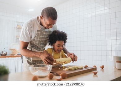 Happy Smiling African American Father and son Cooking and kneading dough on wooden table, Black African male and his boy having fun playing while preparing food in kitchen together - Powered by Shutterstock