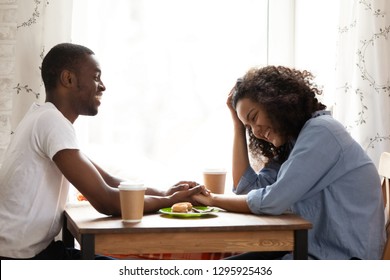 Happy smiling African American man on first date with attractive mixed race girlfriend in cafe, young couple in love laughing at funny joke together, drinking coffee, flirting, pleasant conversation