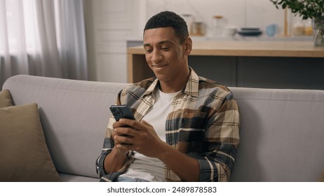 Happy smiling African American man relax on sofa at home smile laugh looking mobile phone screen smartphone chat browsing telephone ethnic guy biracial male watching funny video online fun laughing - Powered by Shutterstock