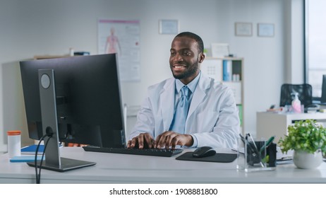 Happy Smiling African American Medical Doctor is Working on a Computer in a Health Clinic. Physician in White Lab Coat is Browsing Medical History Behind a Desk in Hospital Office. - Powered by Shutterstock