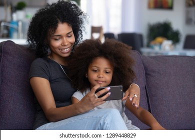 Happy Smiling African American Mother And Little Daughter Taking Selfie On Smartphone, Mixed Race Mom And Child Girl Making Video Call On Cellphone, Mommy Kid Watch Cartoons Using Phone App At Home