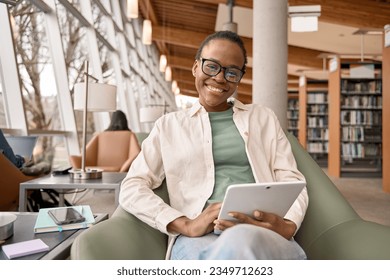 Happy smiling African Black girl student wearing eyeglasses using pad looking at camera, holding digital tablet computer modern tech device elearning sitting in university campus. Portrait. - Powered by Shutterstock