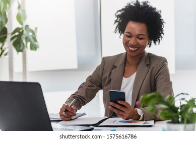 Happy smiling african-american business woman working on laptop at office. Businesswoman sitting at her working place