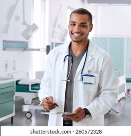 Happy smiling afro american doctor at hospital room with tablet, Looking at camera, standing, wearing stethoscope and lab coat.