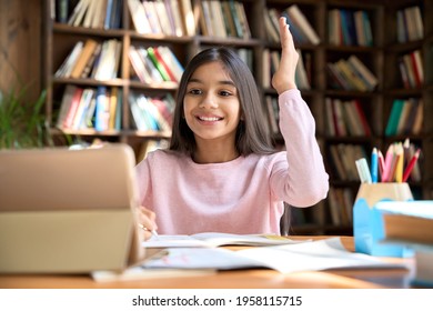 Happy Smiling Arab Indian Girl Student Attending Learning Video Class Webinar In Virtual Classroom On Digital Tablet Device. Latin Spanish School Girl Raising Hand On Virtual Zoom Lesson.