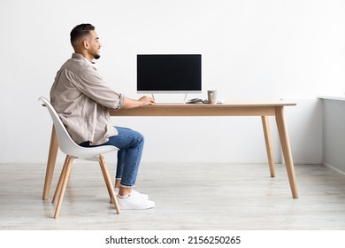 Happy Smiling Arab Man Sitting At Desk At Home Office Using Pc Computer With Blank Black Screen For Mock Up Template, Free Copy Space, Rear Back View. People, Technology, Remote Work Concept