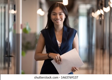 Happy Smiling Asian Businesswoman Looking At Camera Holding Papers Stand In Office Hallway, Happy Confident Chinese Professional Executive Satisfied With Good Career Posing In Modern Office, Portrait