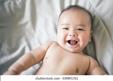 happy smiling asian child in bed over gray.