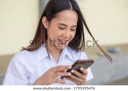 Happy smiling Asian female college student while using smartphone on campus outdoors.