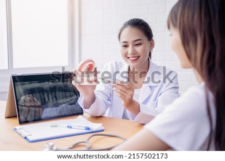 Happy smiling Asian female dentist doctor examining teeth model diagnosing patient dental hygiene using tablet x-ray technology, healthcare expert orthodontist specialist hospital meeting office room 