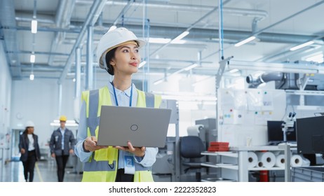 A Happy And Smiling Asian Female Engineer In White Hard Hat Standing With Laptop Computer At Electronic Manufacturing Factory. Successful Employee Watching The Work Flow