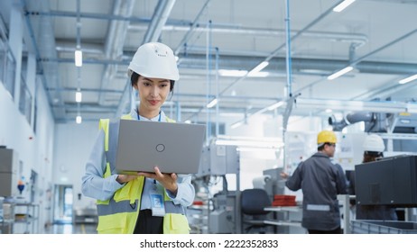 A Happy And Smiling Asian Female Engineer In White Hard Hat Standing With Laptop Computer At Electronic Manufacturing Factory. Successful Employee Focusing On PC Screen