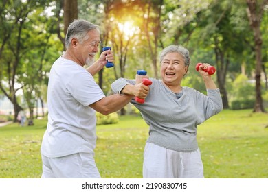 Happy And Smiling Asian Senior Couple Doing Arm Work Out And Lifting Dumbbell Exercise With Relaxation For Healthy In Park Outdoor After Retirement. Health Care Elderly Outdoor Lifestyle Concept.