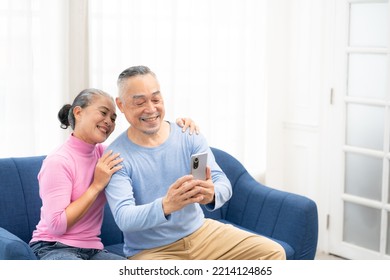 Happy Smiling Asian Senior Couple Sitting On Sofa And Using Smartphone For Online Video Call At Home Living Room. Smiling Mature Video Call Conference Talk Chat Online Concept.